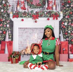 a woman sitting next to a child in front of a fire place with christmas decorations