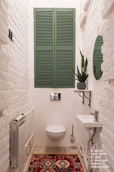 a bathroom with green shutters and a rug on the floor in front of it