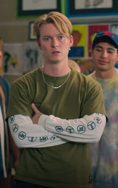 three young men standing in front of a wall with pictures on it and one holding his arms crossed