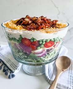 a large glass bowl filled with salad on top of a table next to a wooden spoon