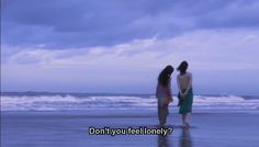 two women standing on the beach looking out at the water and clouds in the sky