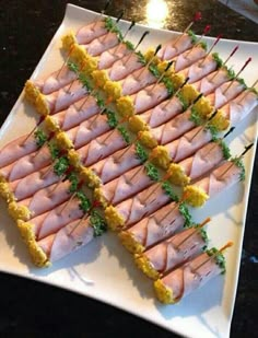 there are many small sandwiches on the white plate with green garnishes and toothpicks