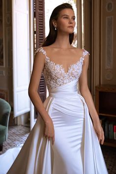 a woman in a white wedding dress standing next to a chair and looking off into the distance