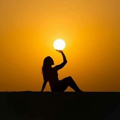 a woman sitting on top of a sandy beach holding a ball in her right hand