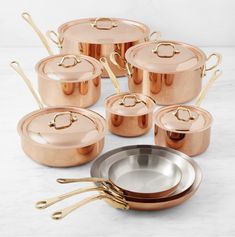 copper pots and pans with gold handles on a marble countertop in front of white background