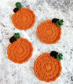 three crocheted pumpkin coasters sitting on top of a marble surface with leaves