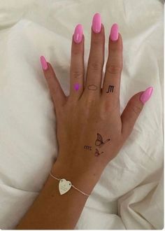 a woman's hand with pink nail polish and tattoos on her left wrist, resting on a white sheet