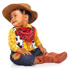 a little boy sitting on the ground wearing a cowboy hat and scarf with his mouth open