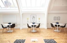 an empty room with tables and chairs in the center, white walls and wood floors