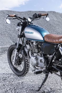 a blue and silver motorcycle parked on top of a gravel field next to a mountain