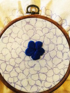 a close up of a small blue flower on a white and brown cloth with a wooden frame