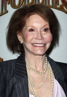 an older woman in a pinstripe suit and pearl necklace smiling at the camera