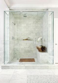 a walk in shower sitting next to a white tiled wall and floor with a vase on the side