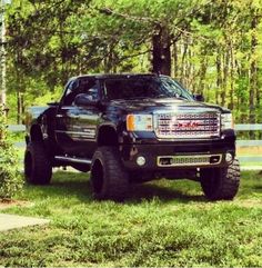 a black truck is parked in the grass near some trees and fenced in area