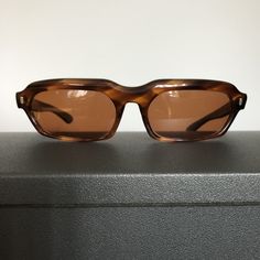 "There's really nothing quite like the original! These sunglasses, with wide tortoiseshell frames in a modified rectangular shape, exude total coolness. The tortoiseshell color is classic and versatile, but these are by no means ordinary sunglasses! Their design suggests that they date from the 1960s, and they have a nice weight that you don't find in the cheaper sunglasses made today. These SunModes sunglasses were manufactured by Styl-Rite Optics, Inc., an American company based in Flushing, New York and incorporated in 1956. Styl-Rite Optics, Inc. should not be confused with Stylrite Optical Industries, founded in India in 1966, or Styl-Rite Optical Mfg. Co., a New Jersey company begun in 1990. The original \"Styl-Rite\" company, which took a patent on the \"SRO\" label, had a small, qu Flushing New York, Tortoiseshell Sunglasses, Eye Symbol, Tortoise Shell Sunglasses, Cheap Sunglasses, Vintage Eyewear, Eyeglass Case, Fun Earrings, Sunglasses Vintage