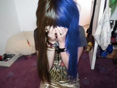 a woman with blue hair covering her face and holding her hand to her face while standing in a room