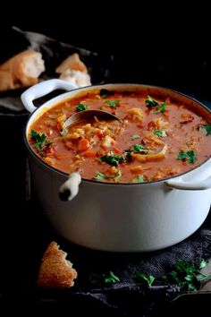 a white pot filled with soup next to bread on a black surface and garnished with parsley