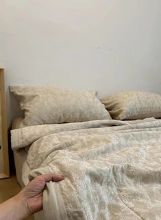 a bed with two pillows on top of it and a person's hand reaching for the pillow