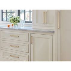 a kitchen with white cabinetry and marble counter tops, along with a vase filled with flowers