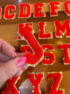 a person holding up a red glittered letter in front of a wooden wall with letters and numbers on it