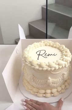 a cake in a box with the word reni on it and someone's hand next to it