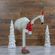 a white flamingo wearing a red and white scarf standing in front of christmas trees