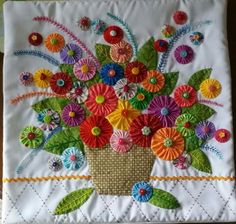 a vase filled with lots of colorful flowers on top of a white table cloth covered in thread