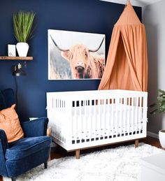 a baby's room with a blue chair, white crib and a cow painting on the wall