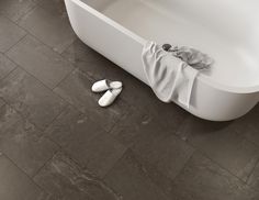 two pairs of slippers sitting on the floor next to a bathtub and towel