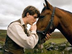 a young man is petting the nose of a brown horse in a grassy field