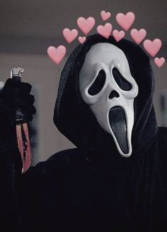 a person wearing a ghost mask and holding a knife in one hand with hearts on the other