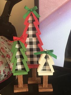 three small wooden christmas trees with green and red bows on them sitting next to each other