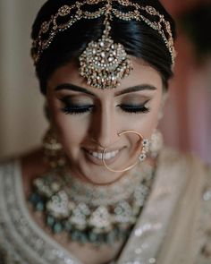 a woman in a bridal outfit with jewelry on her head and nose ring, smiling at the camera