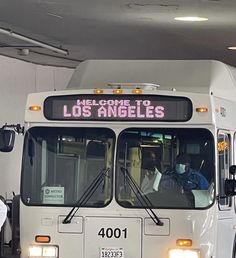 a white bus parked in a garage next to another bus with the words los angeles written on it