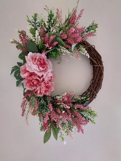 a wreath with pink flowers and greenery hanging on the wall