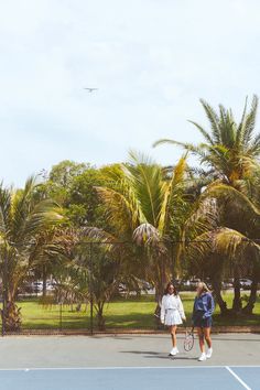 two tennis players walking on the court with their rackets in hand and palm trees behind them