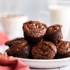 chocolate muffins on a white plate next to a glass of milk and red napkin