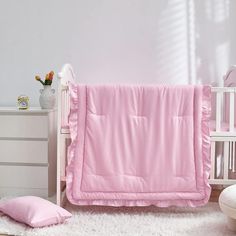 a baby crib with a pink blanket and pillows on the floor next to it