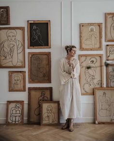 a woman is standing in front of many framed drawings on the wall with her arms crossed