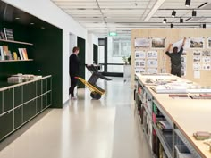 two men are standing in the middle of a room with bookshelves and desks