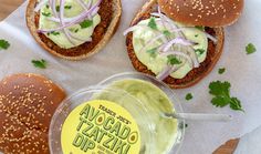 an avocado tasty dip in a plastic container next to three burgers