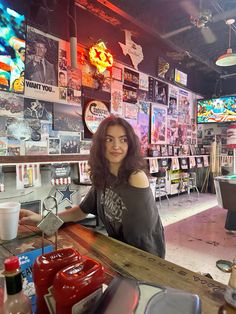 a woman sitting at a bar in front of a wall full of posters and pictures