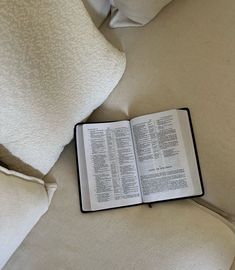 an open book sitting on top of a bed next to pillows and pillow cases with white sheets