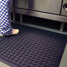 a person wearing checkered pants standing on a mat in front of an oven door