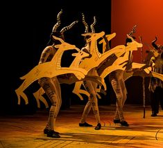 three people are performing on stage with wooden sculptures