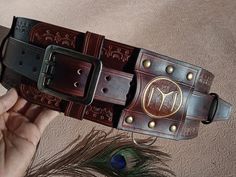 a person holding up a brown leather belt with an embellishment on the side