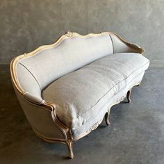 an antique couch with white linen and gold trimmings on the back, sitting against a gray wall