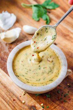 a spoon full of dip being held up over a bowl filled with sauce and garnished with parsley