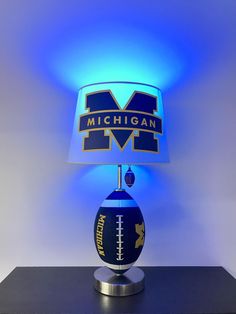 a lamp that is sitting on top of a table in front of a wall with the michigan football logo