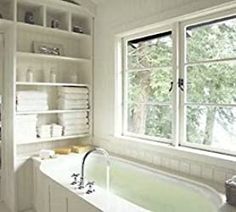 a bath tub sitting under a window next to a sink in a room with white walls